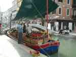 Boat with fruit and vegetables pulled up to sidewalk to sell produce