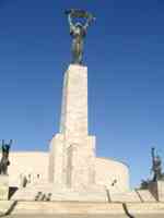 Statue of a woman holding a palm frond overhead on a very tall white stone pedestal